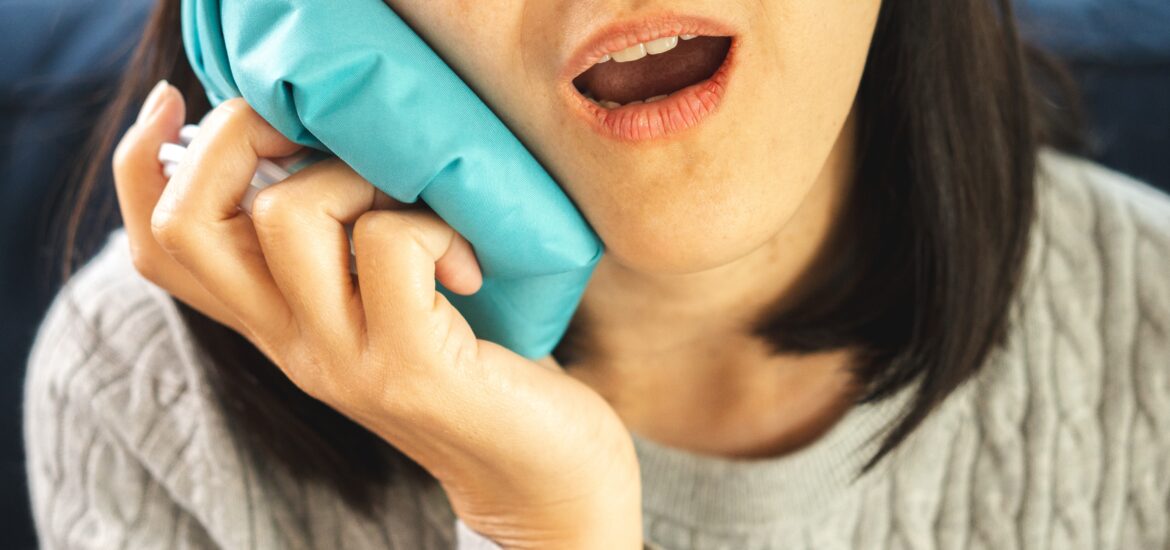 woman suffering from tooth pain and holding a ice pack on her jaw