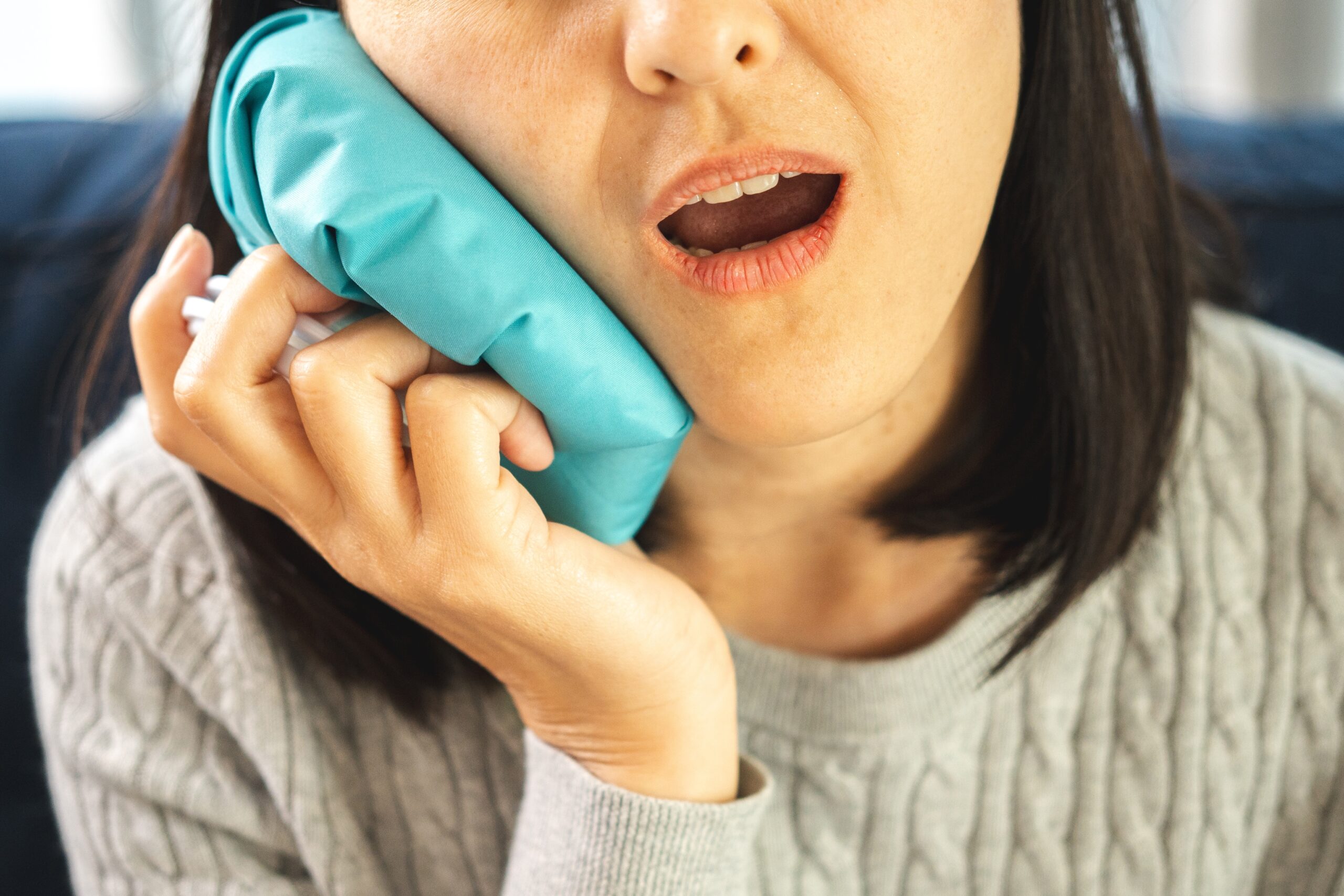 woman suffering from tooth pain and holding a ice pack on her jaw