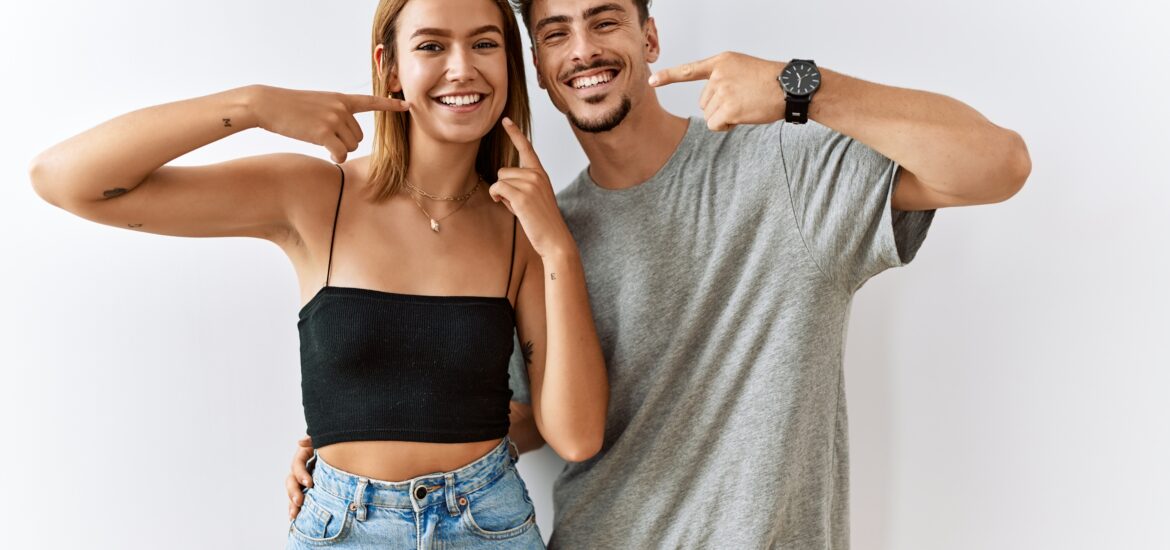 two confident young adults pointing to their perfect smiles